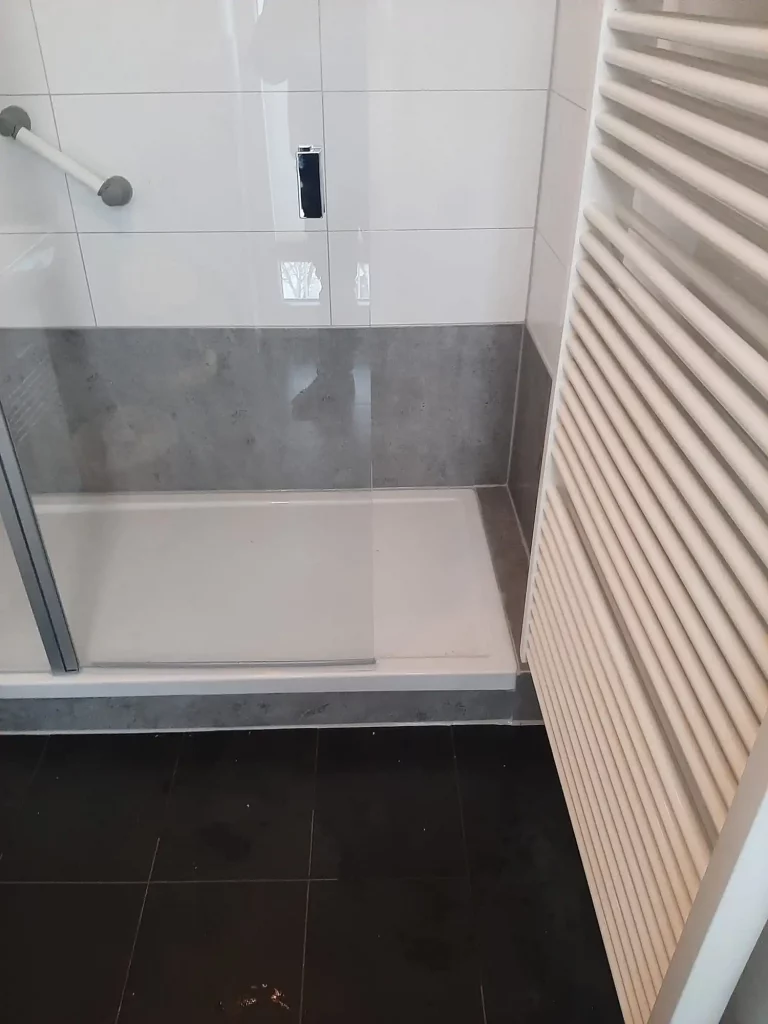 Moderne Dusche mit Glasabtrennung, grauen Fliesen und Handtuchheizkörper in einem Badezimmer. - Praktisches Bad