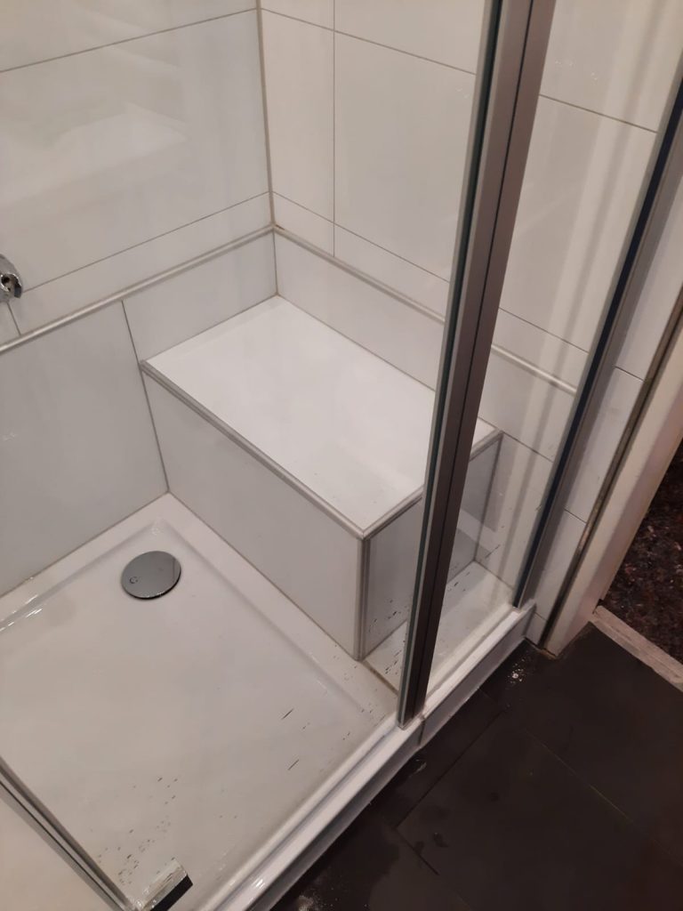Moderne Dusche mit weißen Fliesen und einer Sitzgelegenheit aus Kunststoff im Innenbereich. - Praktisches Bad