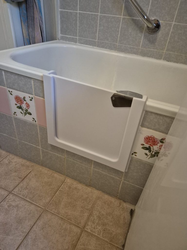 Eine Badewanne mit einem weißen Einstieg, um den Zugang zu erleichtern. Fliesen mit Blumenmuster sind sichtbar. - Praktisches Bad
