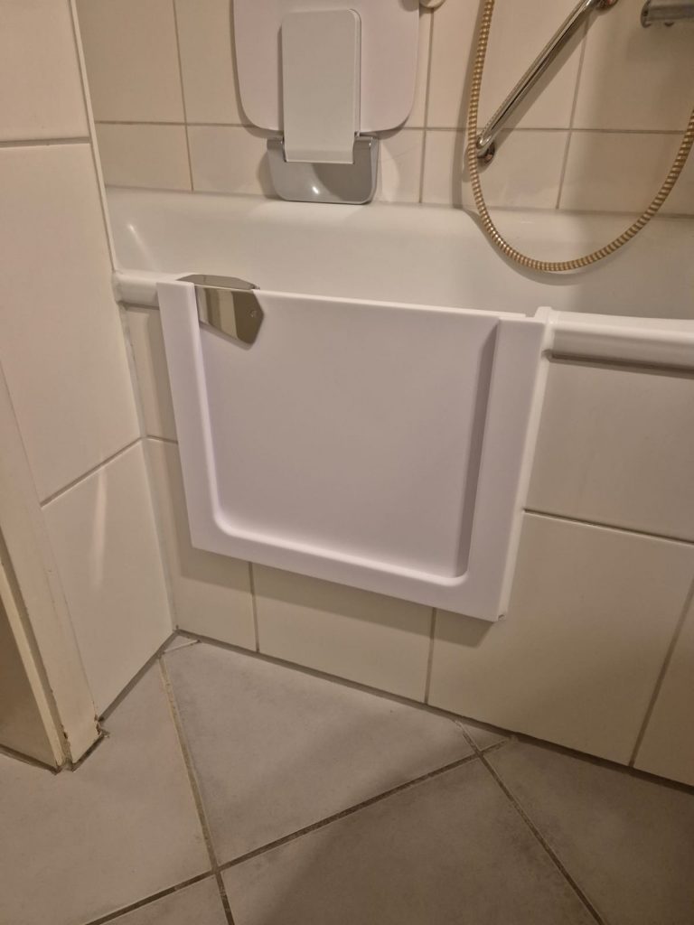 Ein barrierefreier Zugang zur Badewanne mit einer weißen Klappe und einem Haltegriff an der Wand. - Praktisches Bad