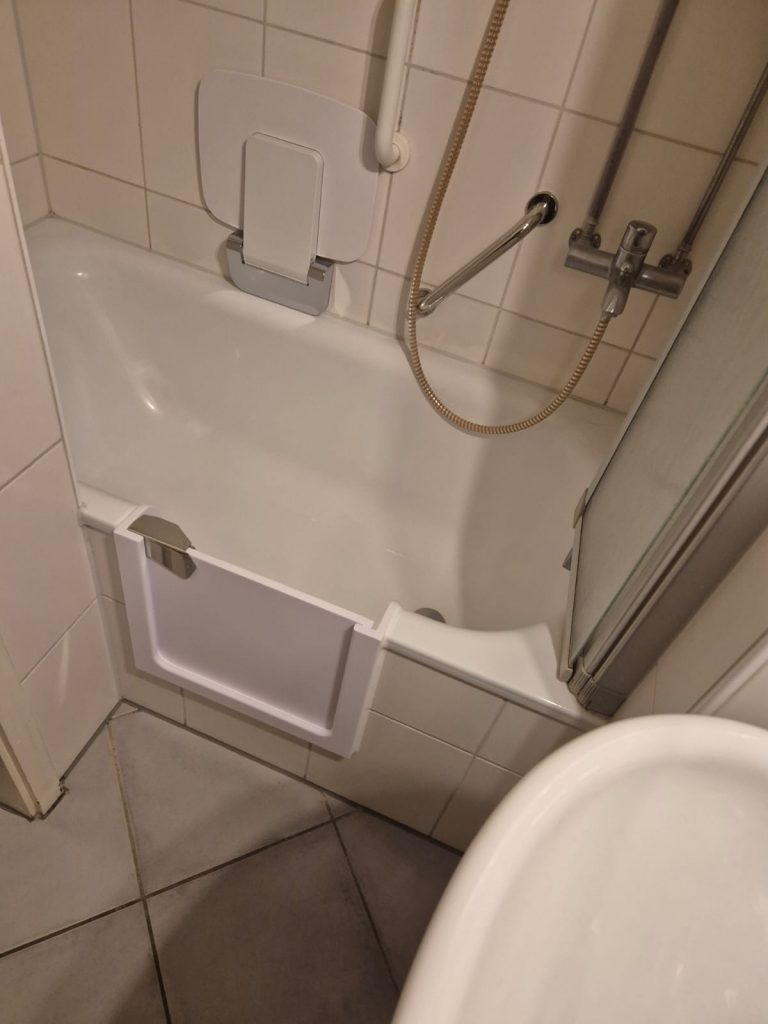 Blick auf eine Badewanne mit einer Duschvorrichtung und einem Zugangselement für einfacheren Einstieg. - Praktisches Bad