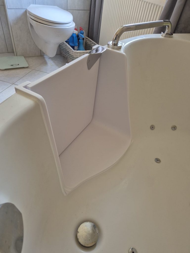 Ein Badezimmer mit einer weißen Badewanne und einem Haltegriff, im Hintergrund eine Toilette und Reinigungsmittel. - Praktisches Bad